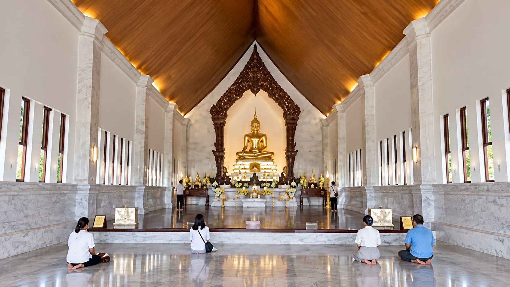 Buddha image and worshippers inside a bright temple hall at the Wat Pa Ban Tat Dhamma Chedi complex.