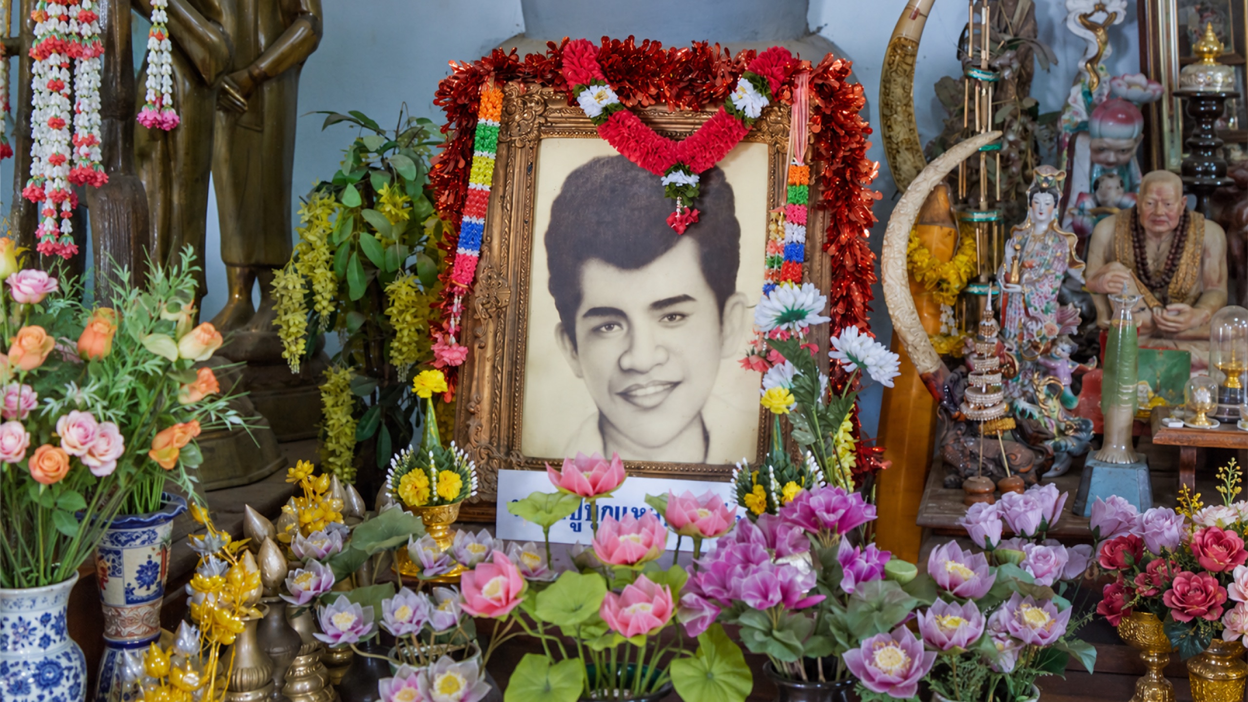 Framed portrait of young Bunleua Sulilat surrounded by offerings and flowers at a shrine altar