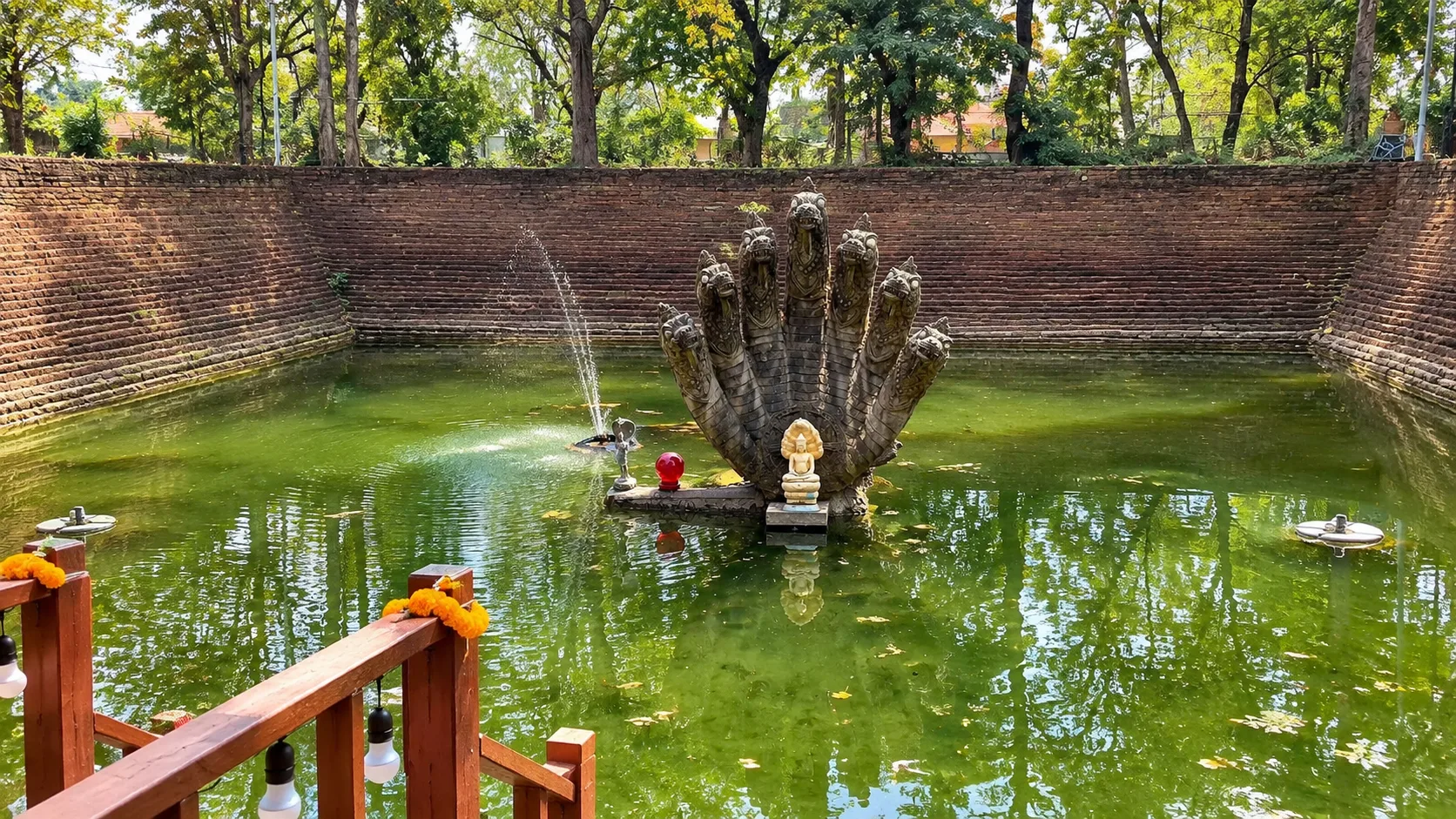 Mucalinda Pond at Wat Phra That Bang Phuan in Nong Khai, with the multi-headed Naga statue rising from the green water inside the brick-lined sacred pond.